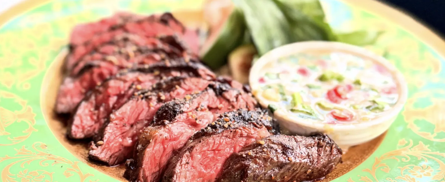 Sliced medium-rare steak finished with a savory sauce on a vintage gold-rimmed green plate at GUSI