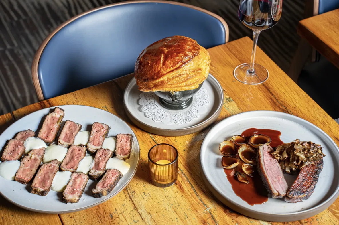 A GUSI dinner of sliced beef, a pastry-topped pot pie, and duck breast in red wine sauce served alongside a glass of natural red wine