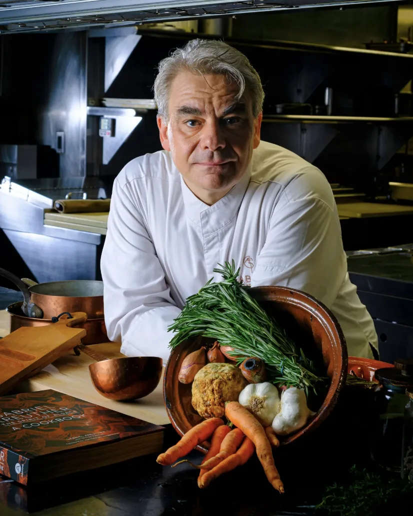 An executive chef in the GUSI kitchen presenting an earthen bowl of root vegetables, fresh rosemary, and seasonal Eastern European ingredients