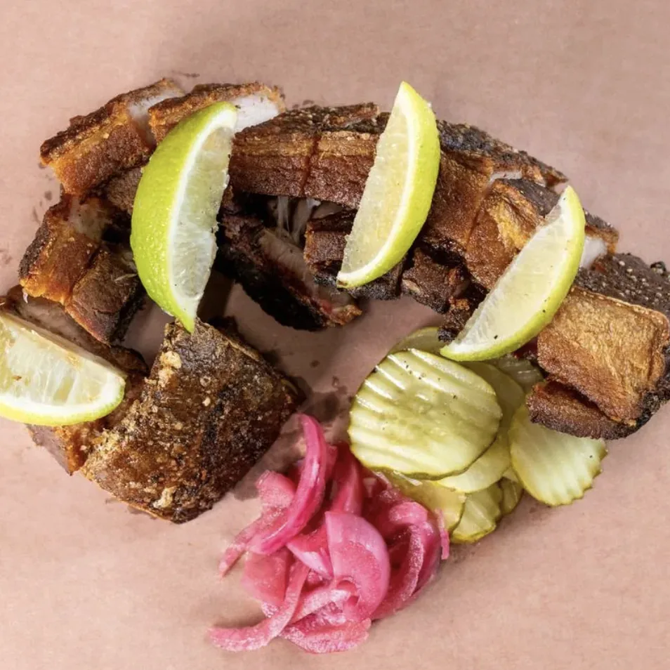 Crispy Eastern European pork belly served with lime wedges, pickled red onion, and house dill pickles at GUSI Restaurant in Greenwich Village