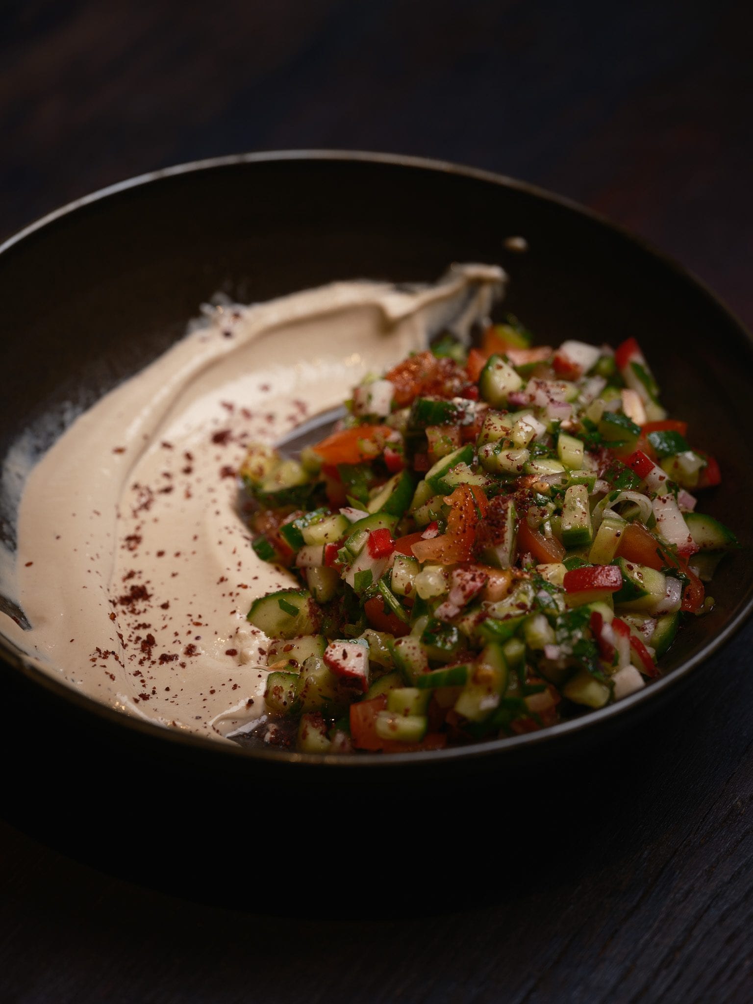 Hummus at GUSI swept across a bowl and topped with a fresh chopped cucumber and tomato salad with sumac
