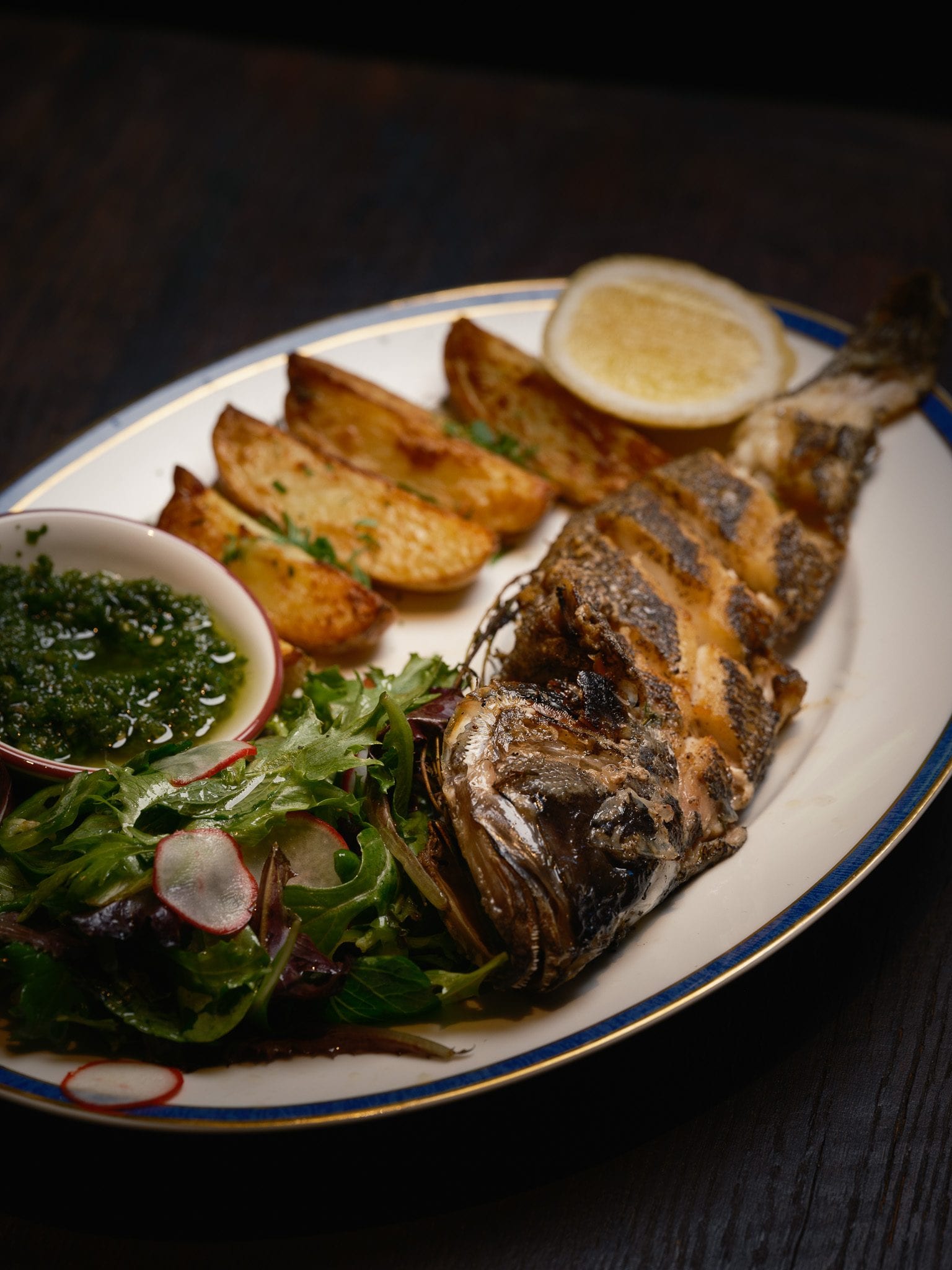 Whole market fish at GUSI, grilled and served with roasted potatoes, green salad, schoug, and lemon