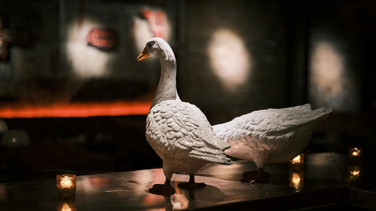 A pair of white porcelain geese on GUSI's first-floor bar in Greenwich Village — the brand's namesake mark beside candles and warm tavern lighting at 432 Sixth Avenue, NYC